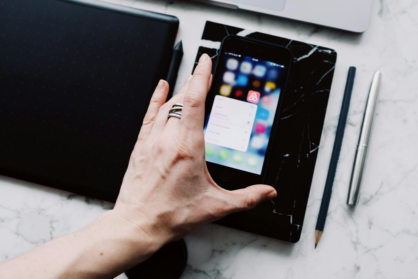 Designer's hand pressing on a smartphone home screen showing an Airbnb app prompt