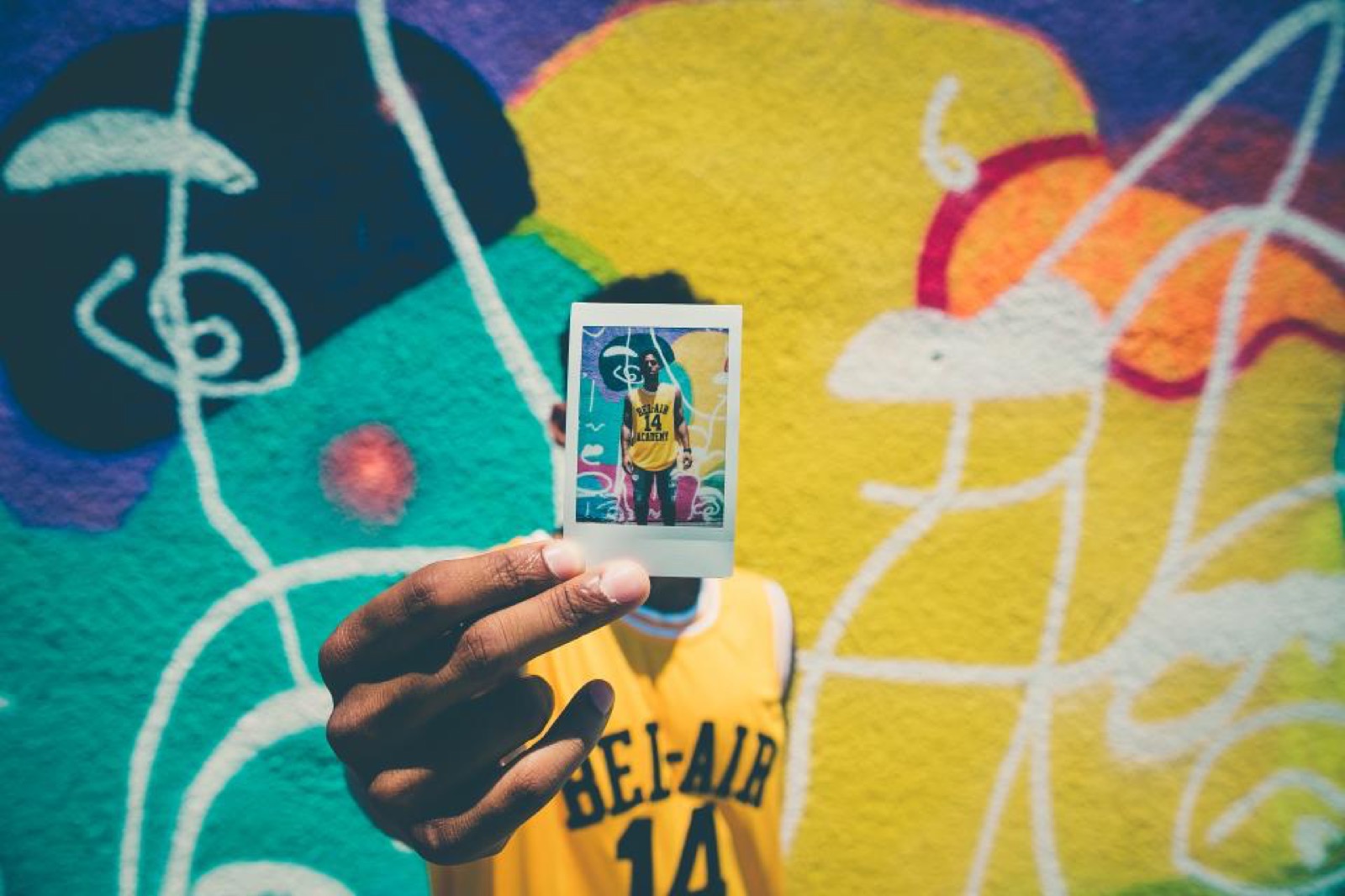 A hand holding a polaroid photo against a graffiti wall