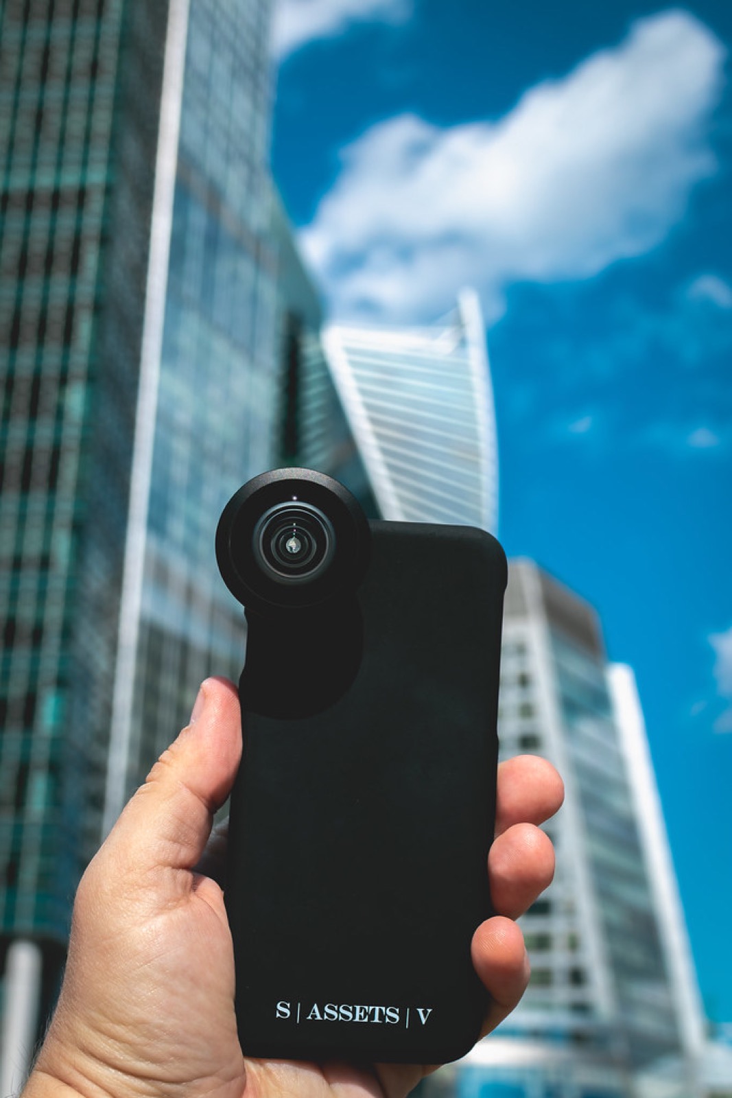 A hand holding a smartphone up against tall buildings