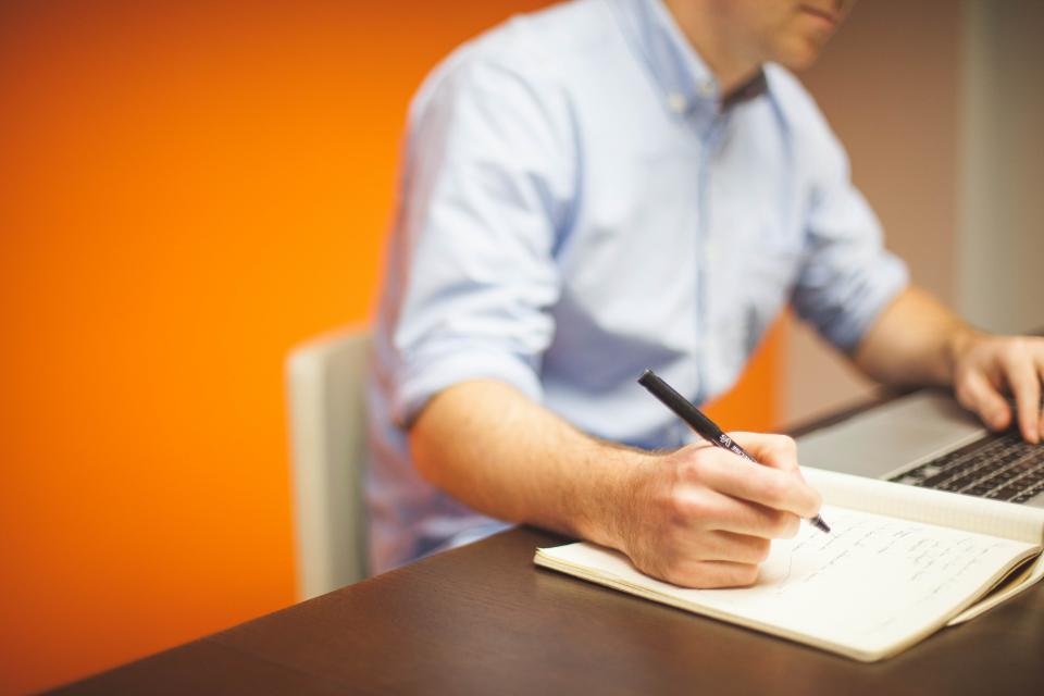 A hand writing in a notebook with a pen
