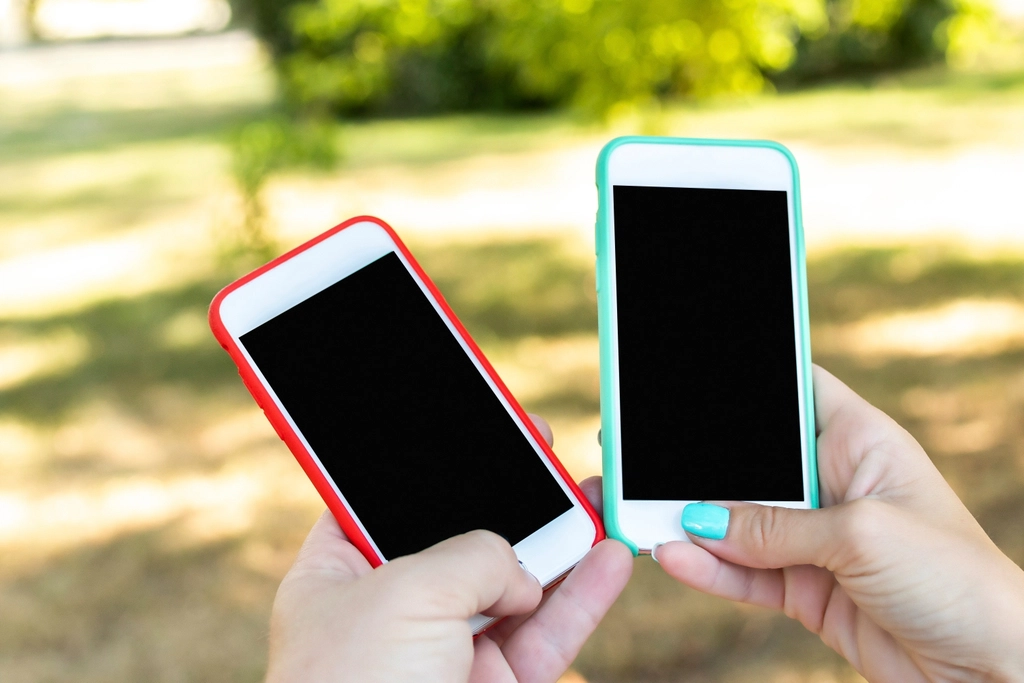 Two smartphones with blank screens held in people's hands