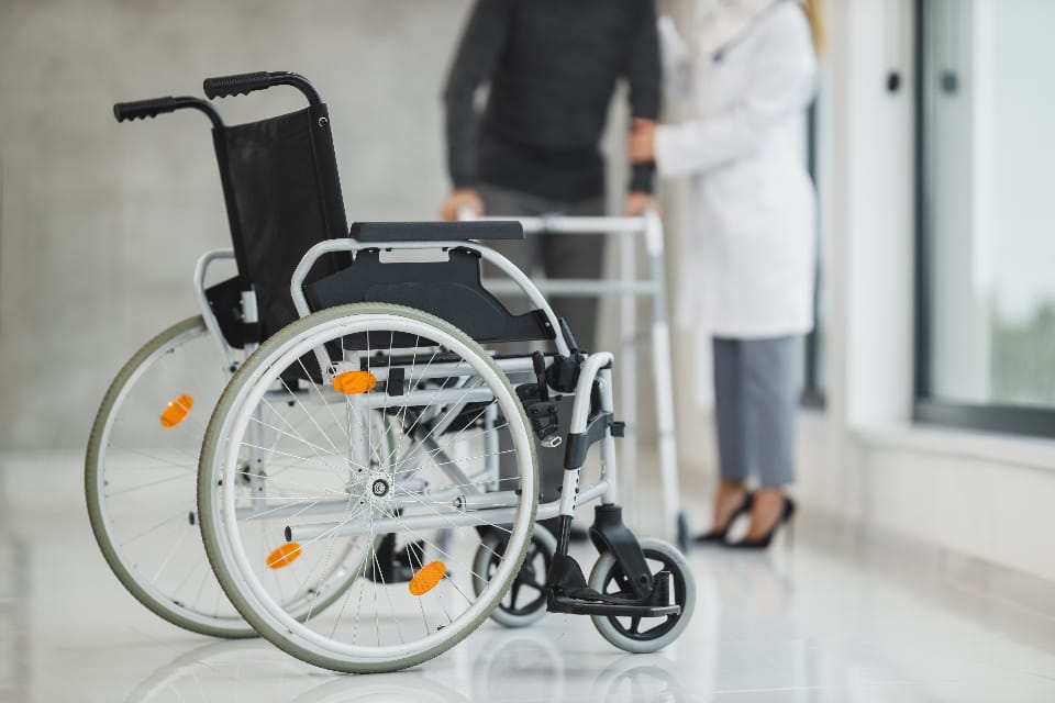 An empty wheelchair in a bright corridor with a clinician and patient behind